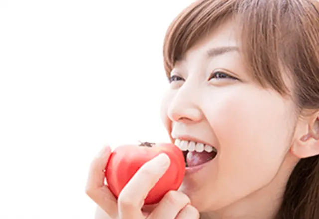 笑顔でトマトをまるかじるする女性の画像